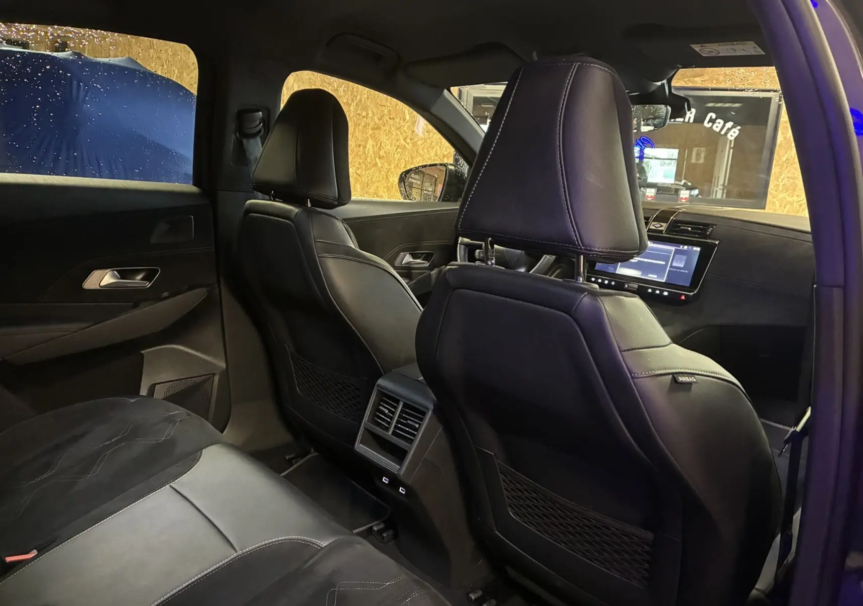 Vue intérieure arrière du DS7 E-TENSE 2024 avec sièges en cuir noir et écran tactile visible au tableau de bord.