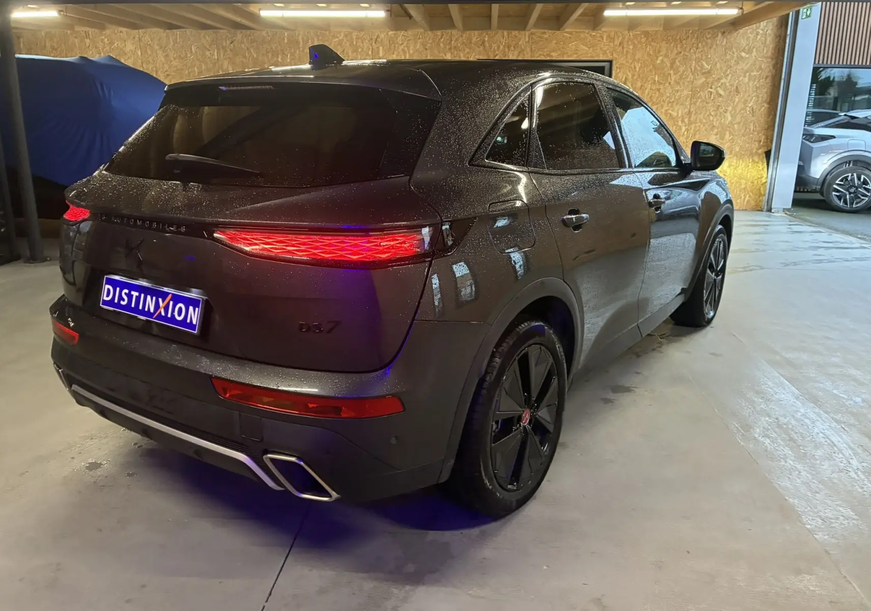 Vue 3/4 arrière droite du DS7 E-TENSE gris avec feux arrière allumés et double sortie d’échappement intégrée.