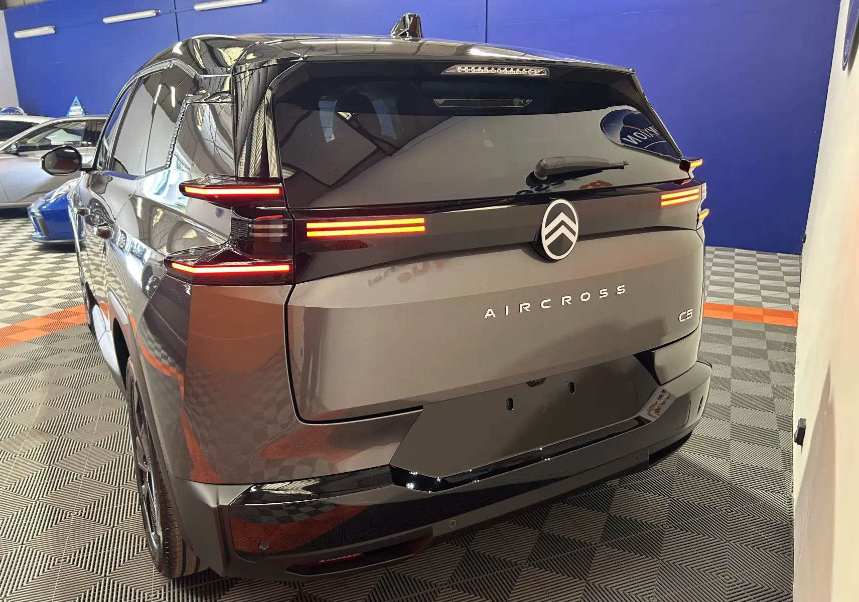 Vue 3/4 arrière droite du Citroën C5 Aircross gris Platinium avec feux arrière LED allumés et toit noir biton.