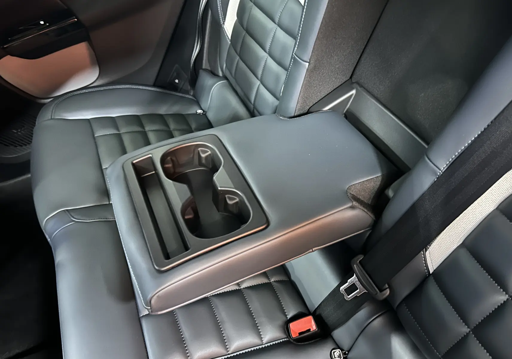 Vue rapprochée de l'accoudoir central arrière avec porte-gobelets sur les sièges en cuir gris du Citroën C5 Aircross II Hybrid.
