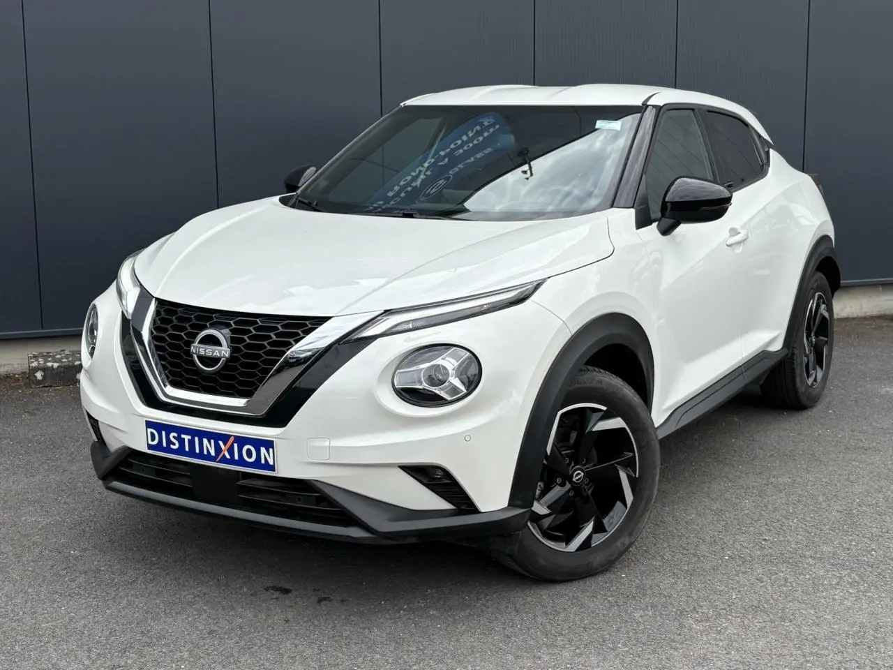 Nissan Juke blanc perle en 3/4 avant droit, avec jantes alliage noires et calandre chromée distinctive.