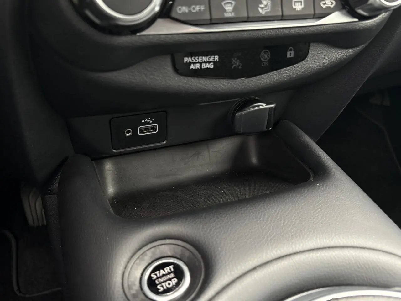 Gros plan sur la console centrale noire du Nissan Juke blanc perle, montrant le bouton Start/Stop et une prise USB.