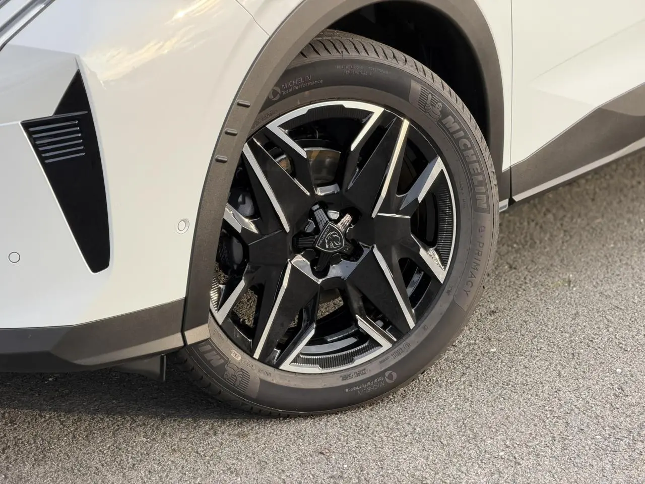 Gros plan sur la roue avant droite du Peugeot 3008 Hybrid blanc Okénite avec jante alliage noire et argentée.