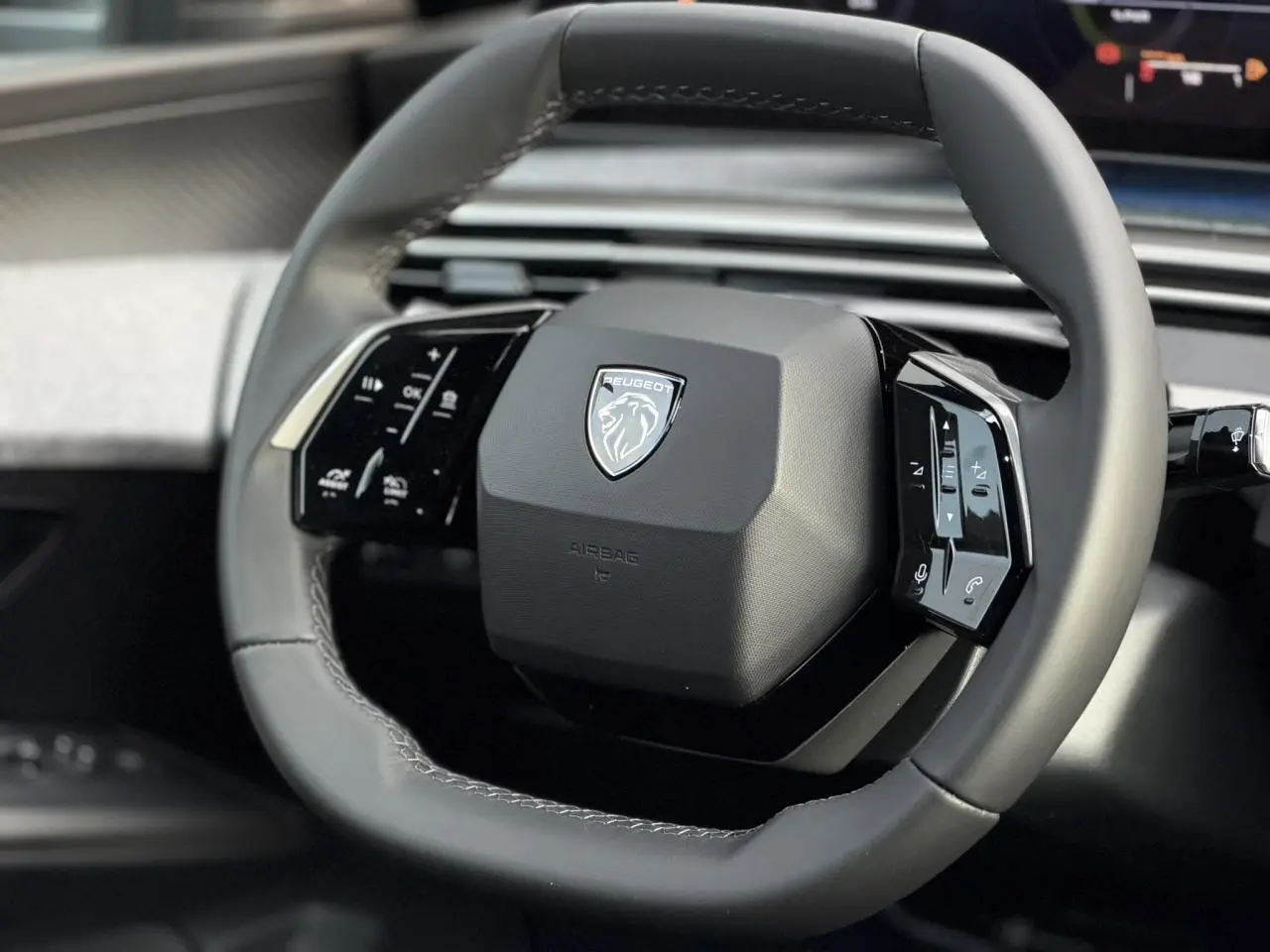 Gros plan sur le volant compact en cuir gris du Peugeot 3008 Hybrid 2025 avec commandes intégrées noir laqué.