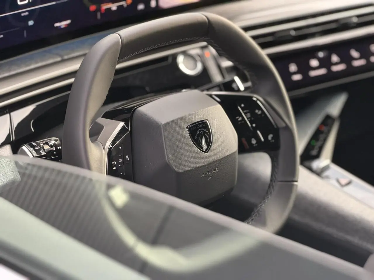 Gros plan sur le volant noir du Peugeot 3008 Hybrid 2025 avec logo lion et tableau de bord numérique en arrière-plan.
