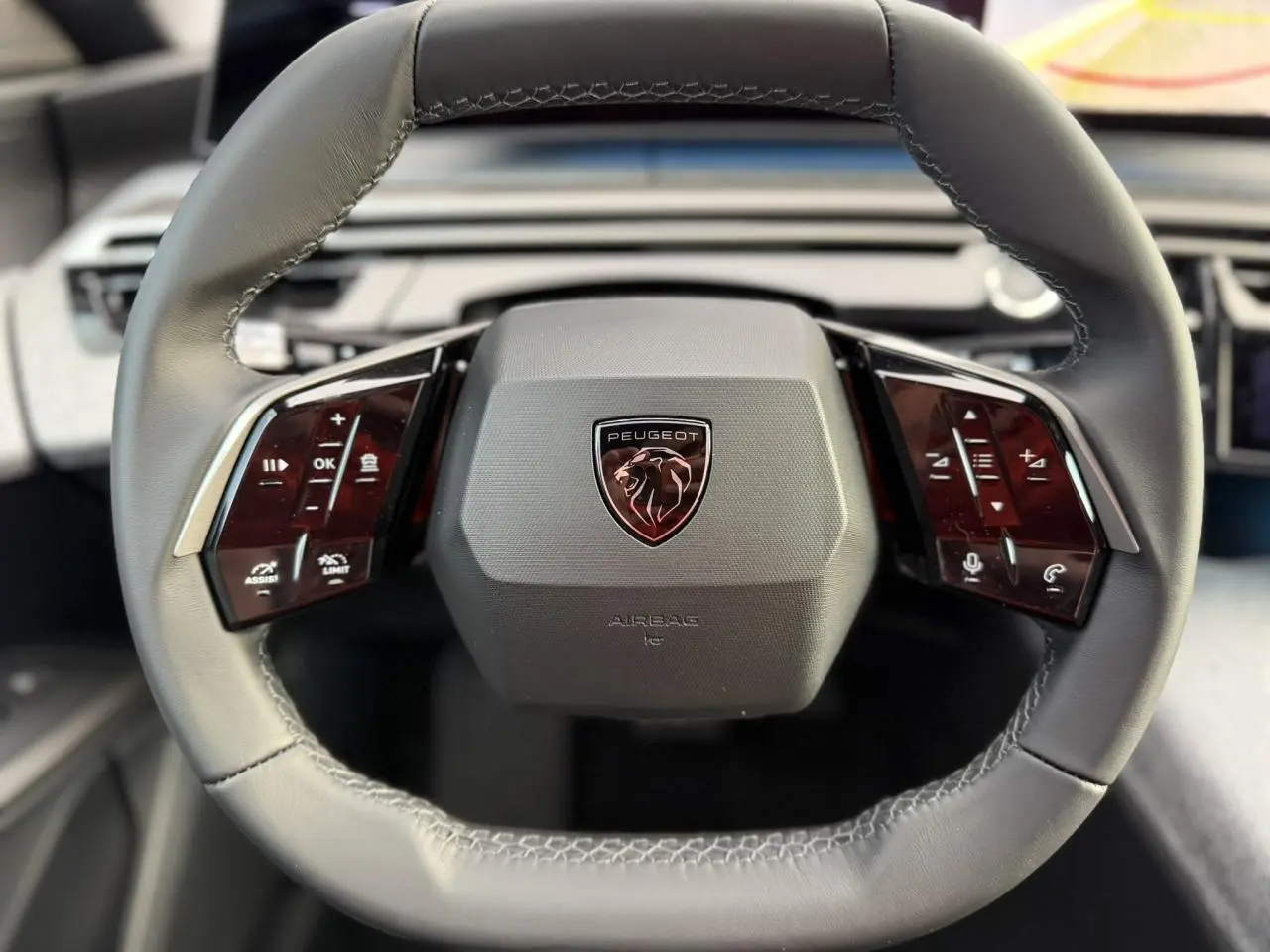 Gros plan sur le volant noir cuir du Peugeot 3008 Hybrid 2025 avec commandes tactiles et logo lion central.