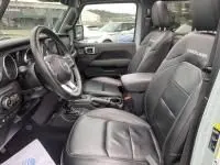 Intérieur de la Jeep Wrangler Unlimited 2023, vue côté conducteur, sièges cuir noirs et tableau de bord moderne.