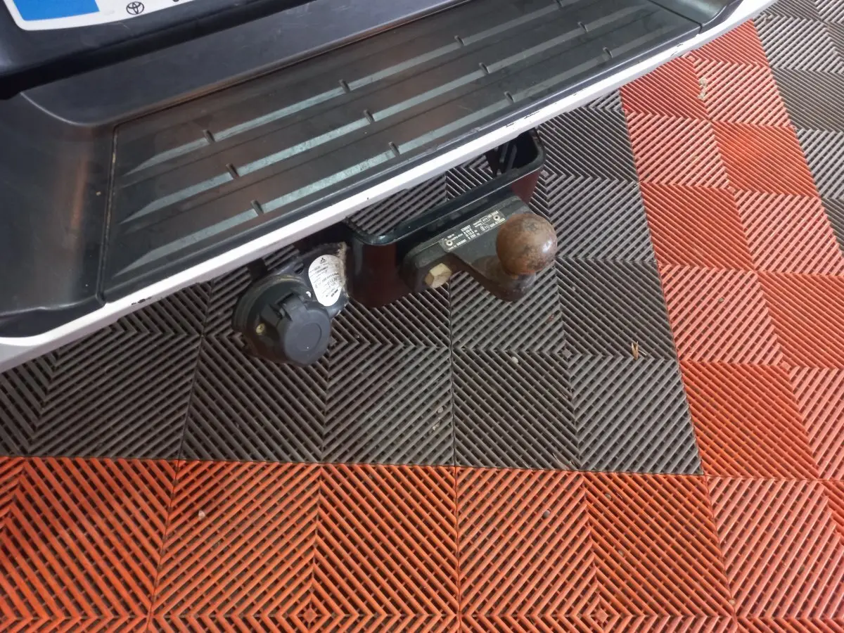 Gros plan sur l'attelage et la prise électrique arrière d'un Mitsubishi L200 gris foncé, vue du dessous du pare-chocs.