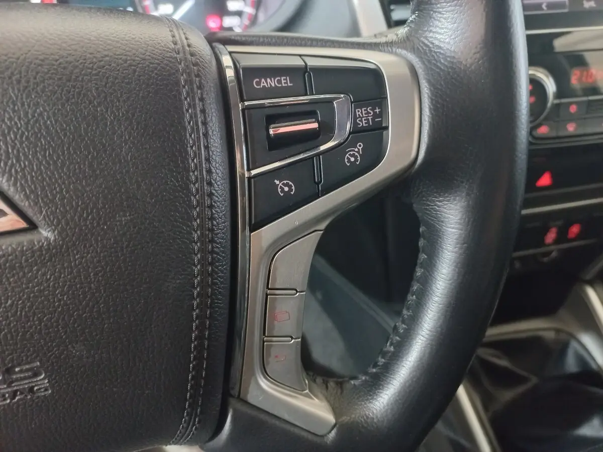 Gros plan sur le volant cuir noir du Mitsubishi L200 2020, avec commandes de régulateur de vitesse intégrées.