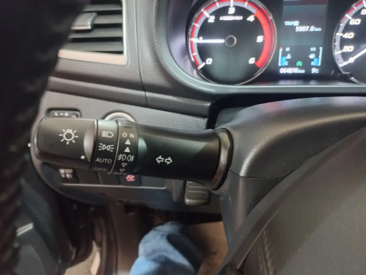 Gros plan sur la manette de commande des phares et clignotants du Mitsubishi L200 gris foncé, tableau de bord en arrière-plan.