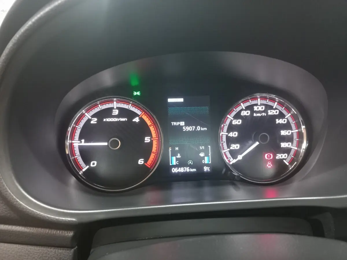 Tableau de bord du Mitsubishi L200 gris foncé 2020, affichage digital central et compte-tours à gauche, compteur de vitesse à droite.