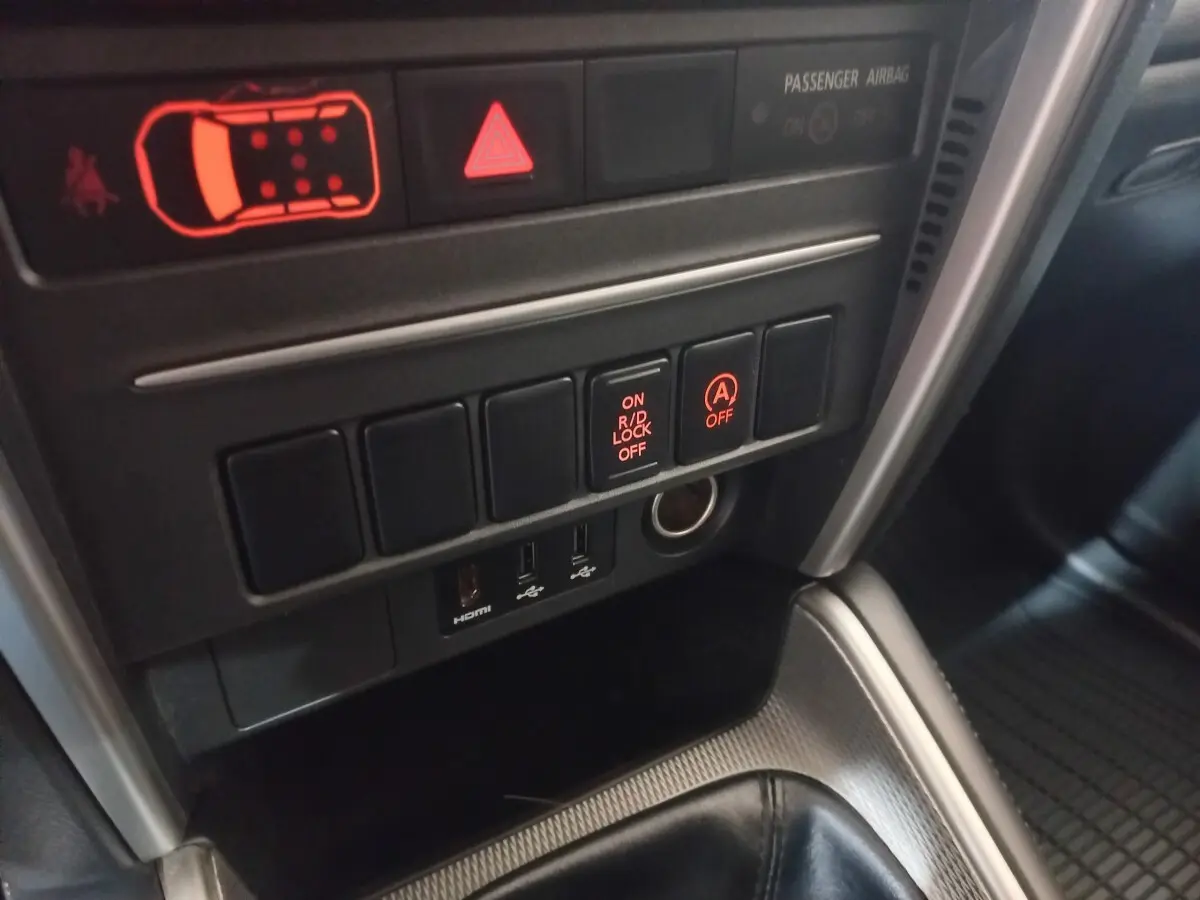 Gros plan sur les commandes centrales du Mitsubishi L200 2020, avec boutons lumineux et prises USB visibles.