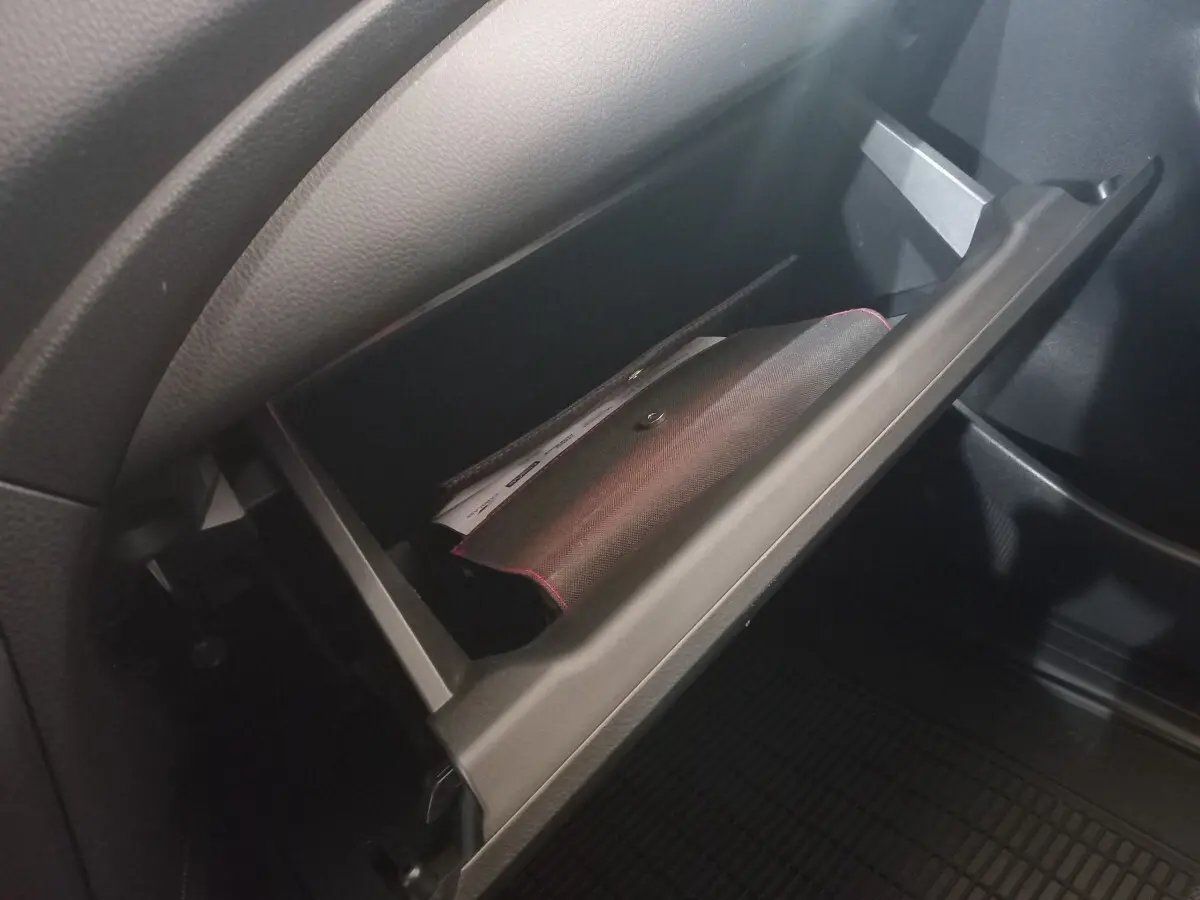 Gant de rangement ouvert côté passager intérieur du Mitsubishi L200 gris foncé, montrant un document à l'intérieur.