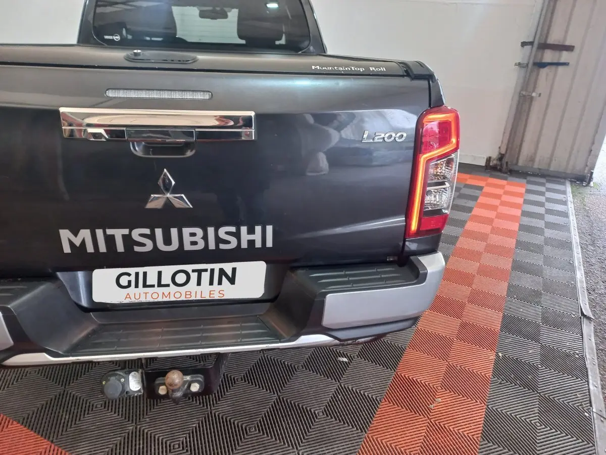 Vue arrière du pick-up Mitsubishi L200 gris foncé avec hayon fermé et feux arrière allumés en intérieur.