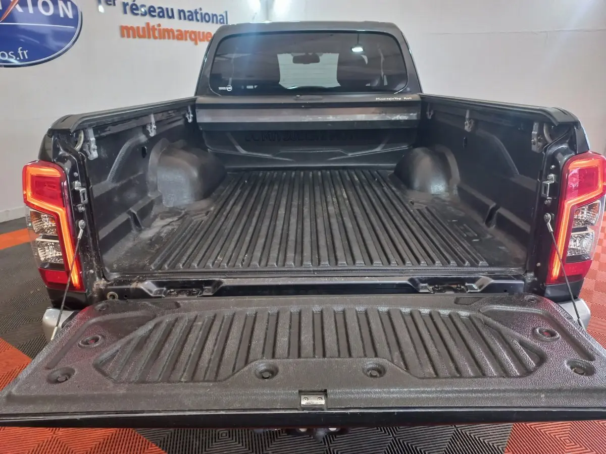 Vue arrière du pick-up Mitsubishi L200 gris foncé avec benne ouverte et ridelles visibles dans un showroom.