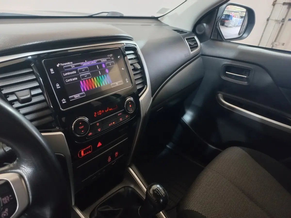 Vue intérieure côté passager du Mitsubishi L200 2020, tableau de bord noir avec écran tactile et levier de vitesses manuel.