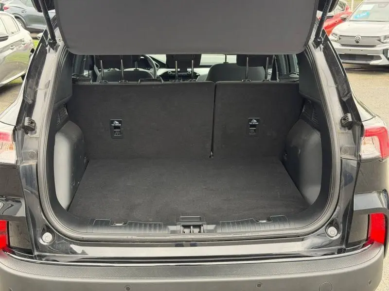 Coffre ouvert vu de l'arrière d'un Ford Kuga 1.5 EcoBoost 150ch Titanium 2024 noir, intérieur spacieux et propre.