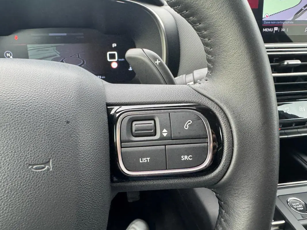 Gros plan sur les commandes au volant du Citroën C5 Aircross 2024 hybride, avec tableau de bord numérique en arrière-plan.