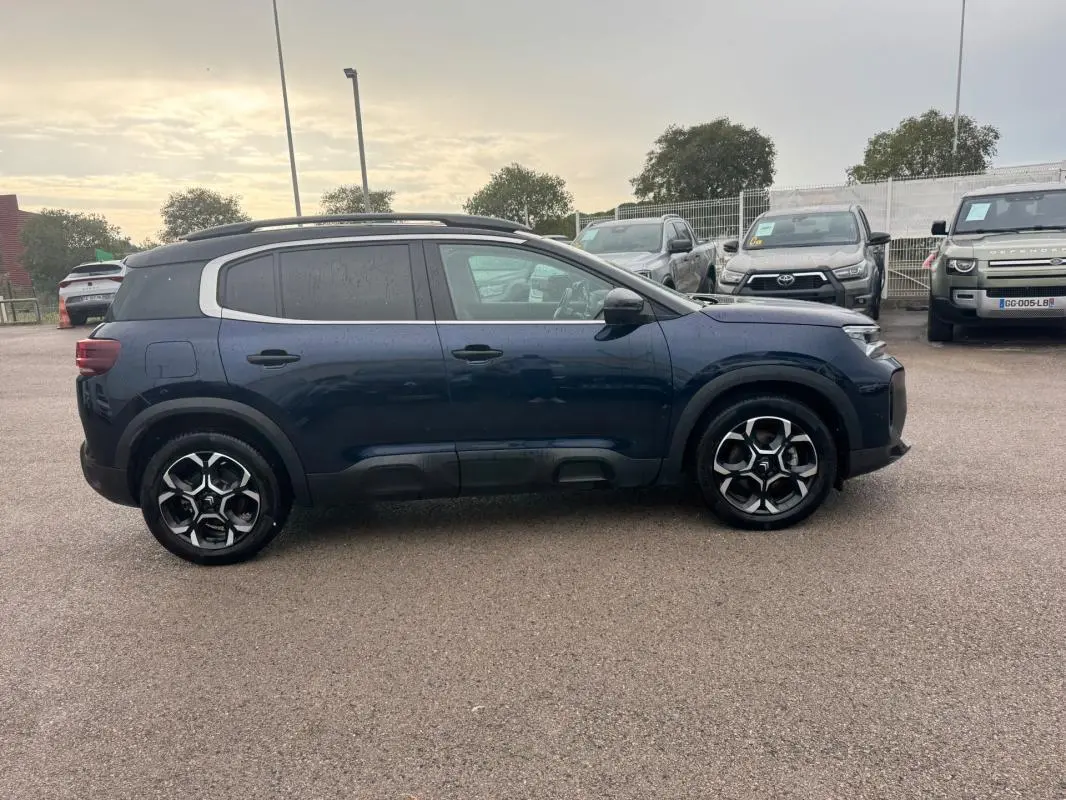 Vue de profil côté gauche d’un Citroën C5 Aircross hybride bleu foncé avec barres de toit et jantes alliage 18 pouces.