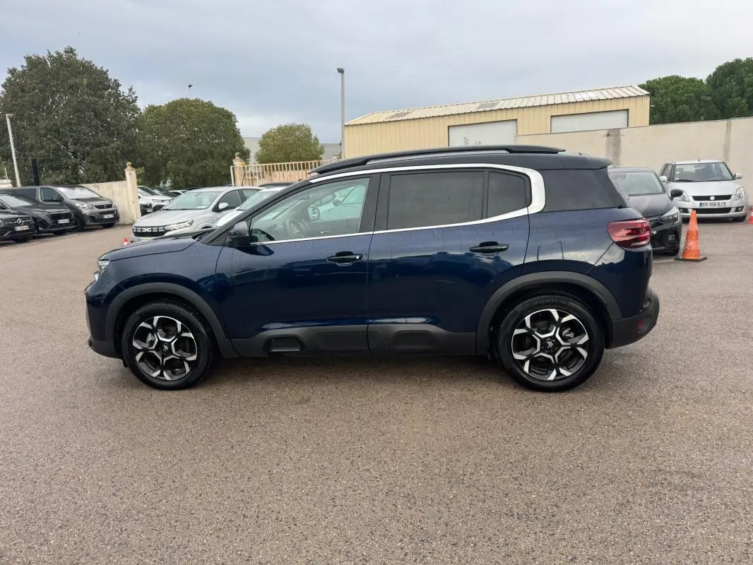 Vue latérale droite d'un Citroën C5 Aircross hybride bleu foncé avec barres de toit et jantes alliage 18 pouces.