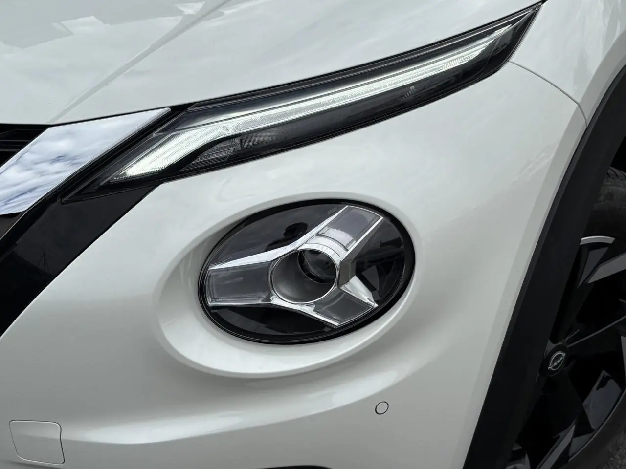 Gros plan sur le phare antibrouillard avant droit du Nissan Juke blanc perle, soulignant ses lignes modernes et la calandre noire.