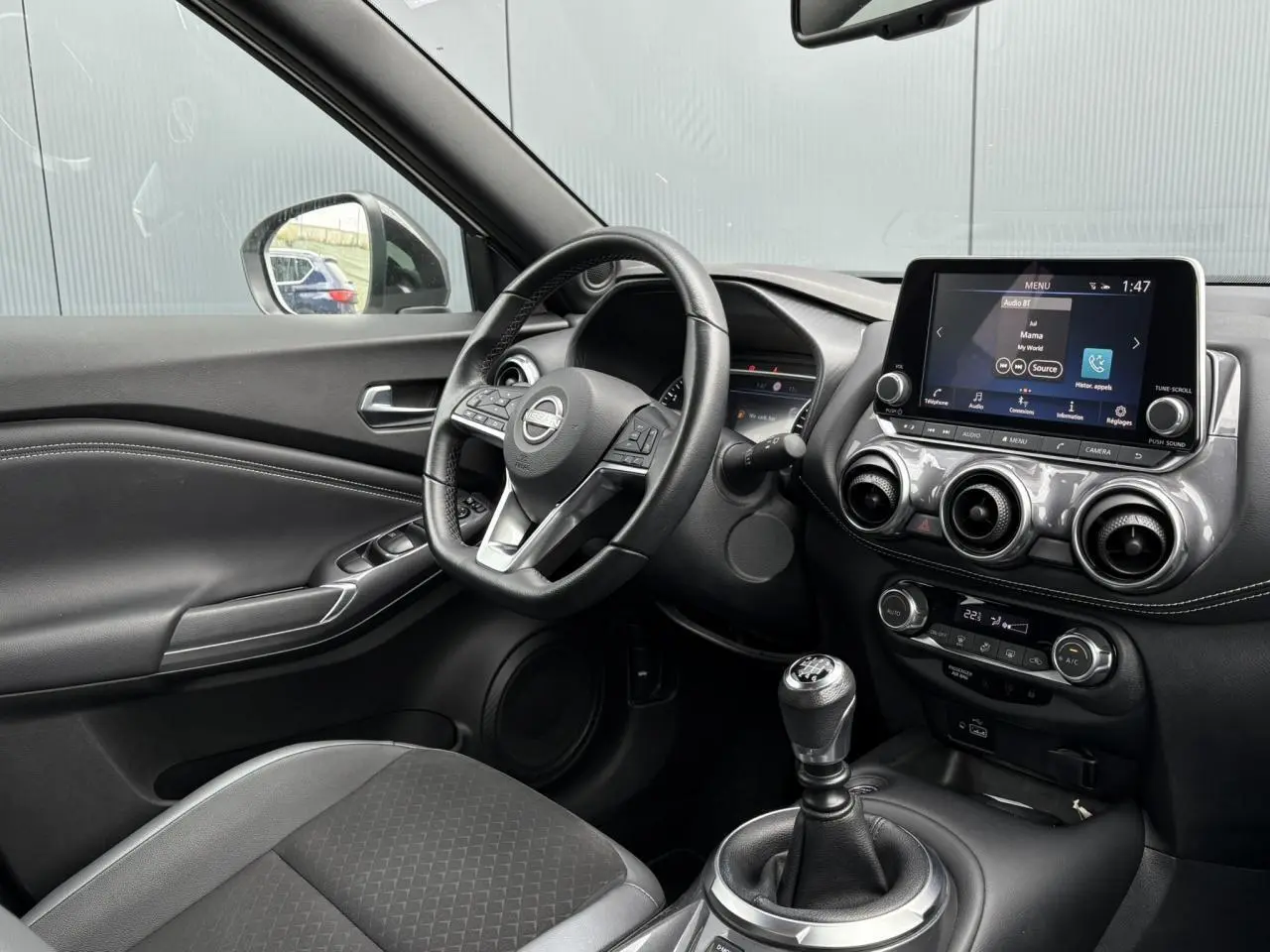 Intérieur du Nissan Juke 2023 vu côté conducteur, volant cuir, écran tactile et levier de vitesse manuel visibles.