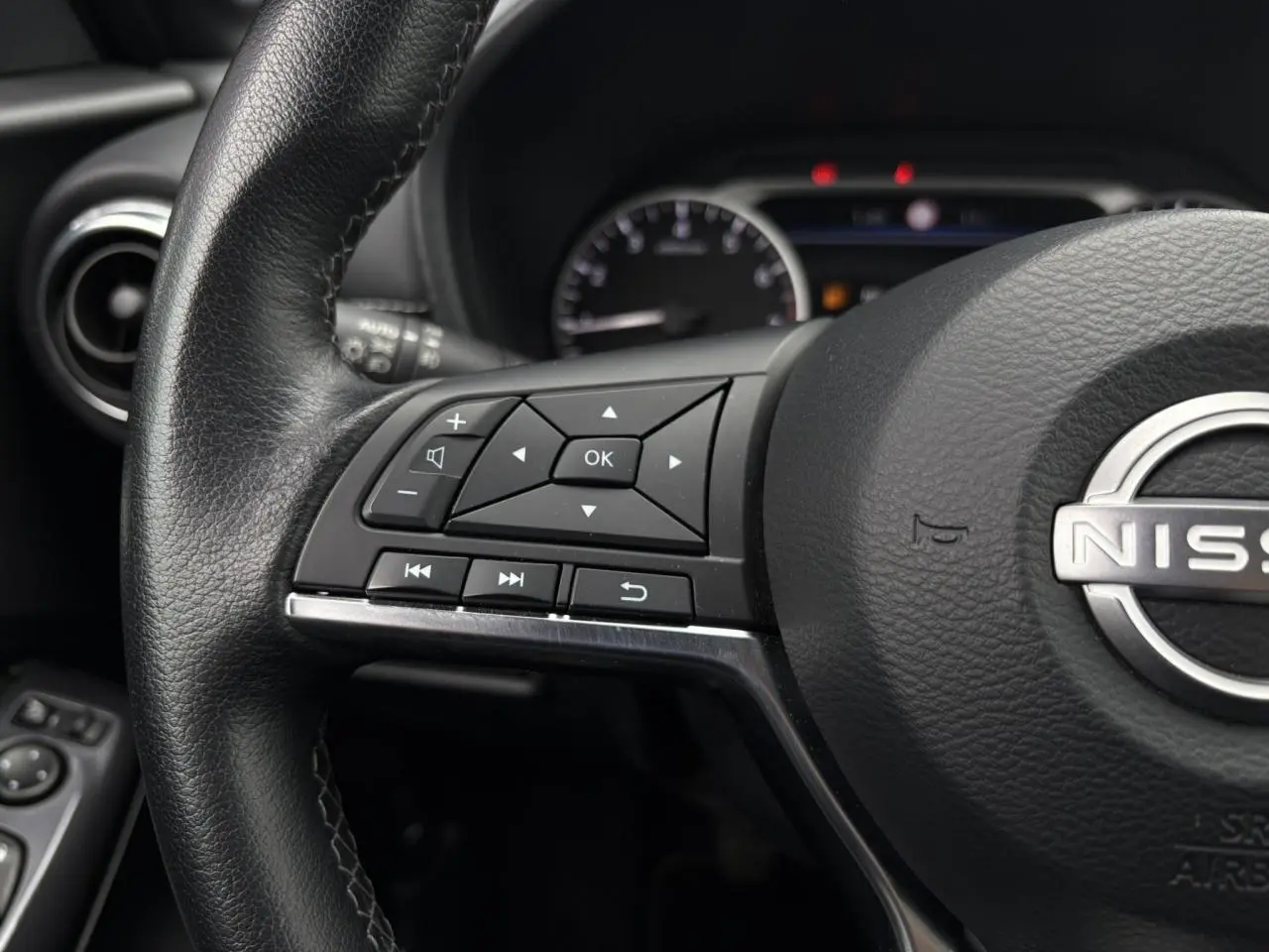 Gros plan sur le volant noir du Nissan Juke 2023 avec commandes intégrées côté gauche et logo central visible.