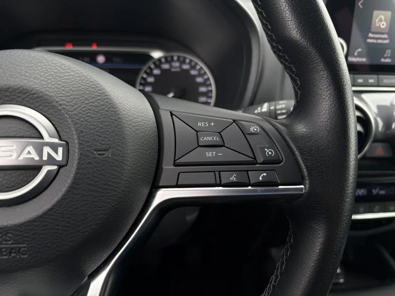 Gros plan sur le volant noir du Nissan Juke 2023, côté droit, avec commandes de régulateur de vitesse et téléphone.