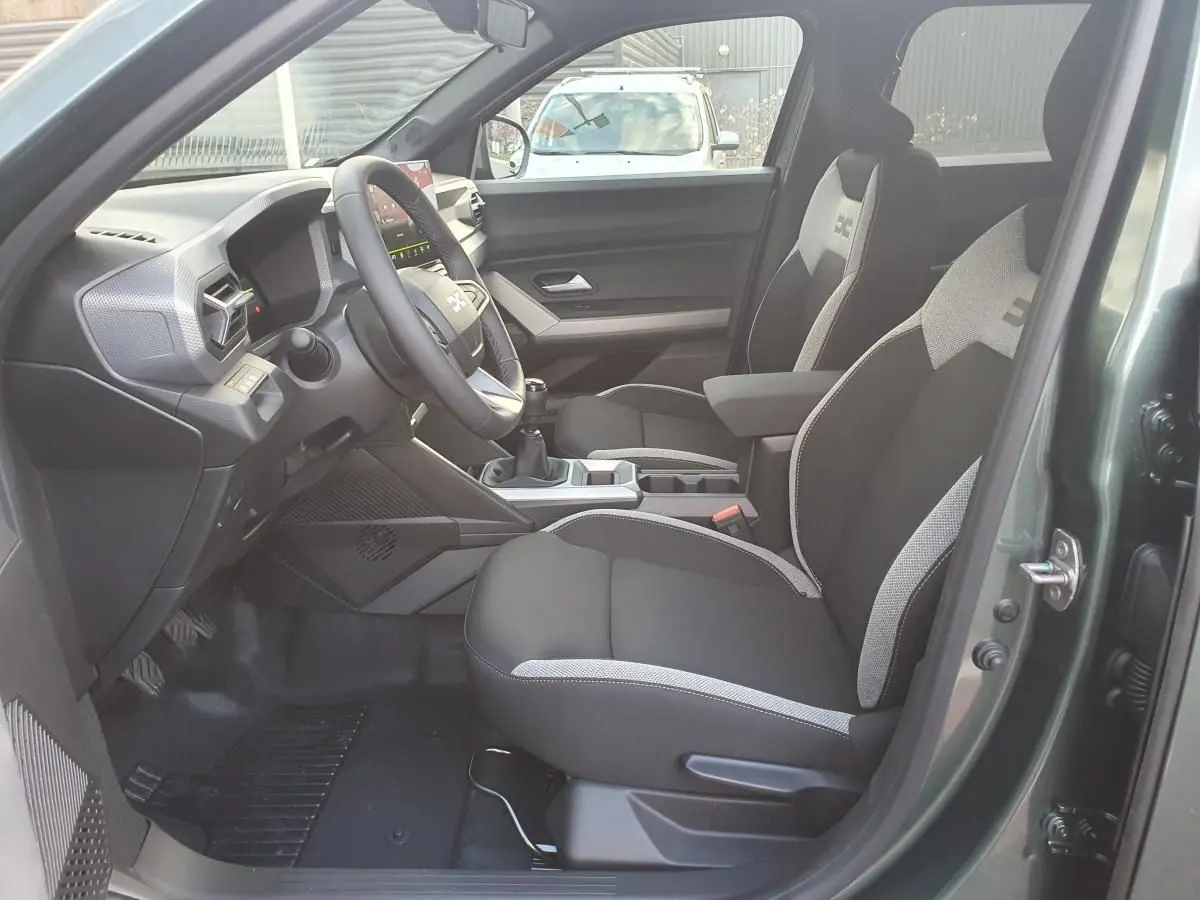 Intérieur du Dacia Duster 2026 vert cèdre, vue côté conducteur, sièges tissu bicolore et tableau de bord moderne.