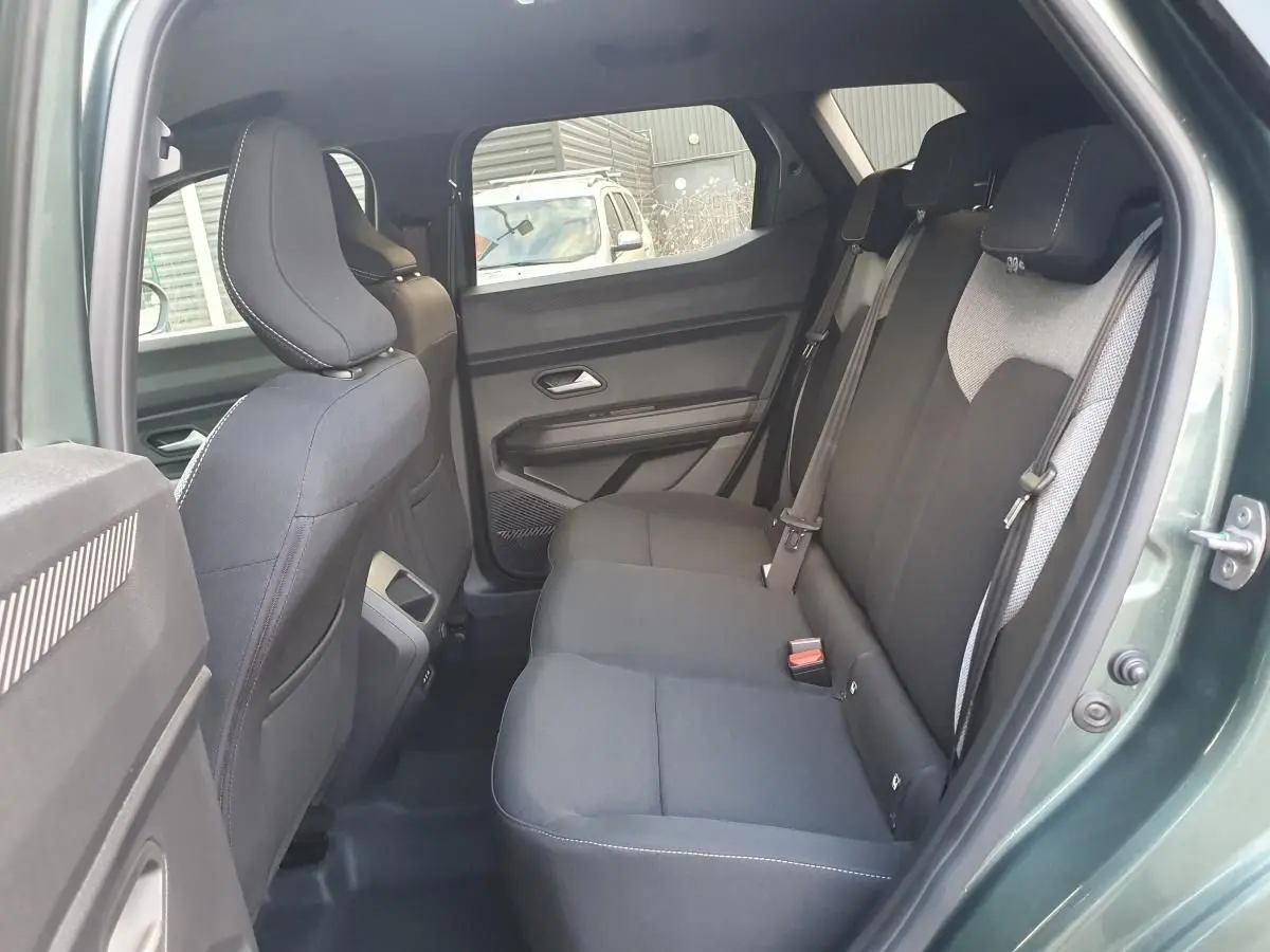 Vue intérieure côté droit de la banquette arrière noire du Dacia Duster vert cèdre avec prises USB à l'arrière de la console.