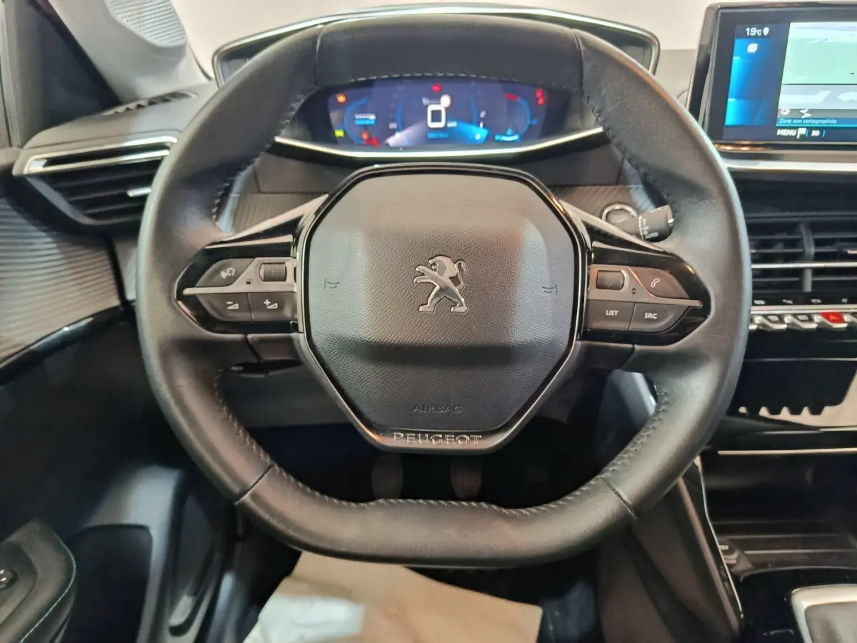 Vue rapprochée du volant cuir noir de la Peugeot 208 avec tableau de bord numérique et écran tactile visible à droite.