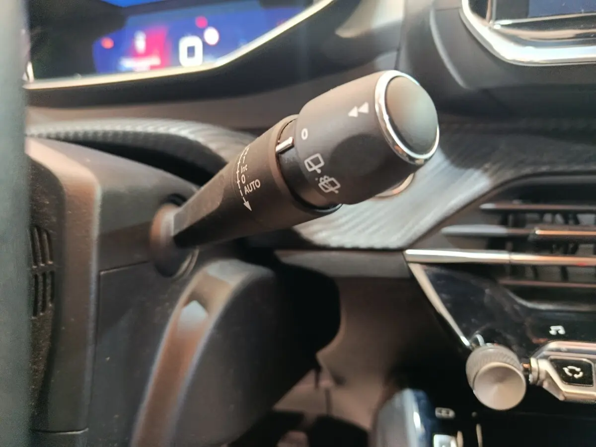 Gros plan sur la commande d’essuie-glace du tableau de bord noir de la Peugeot 208 blanche, version PureTech 100 S&S Allure Business.