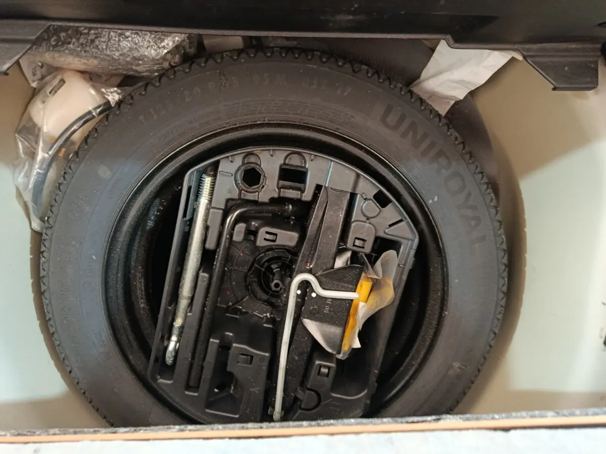 Vue rapprochée de la roue de secours noire et des outils de bord dans le coffre d'une Peugeot 208 blanche.
