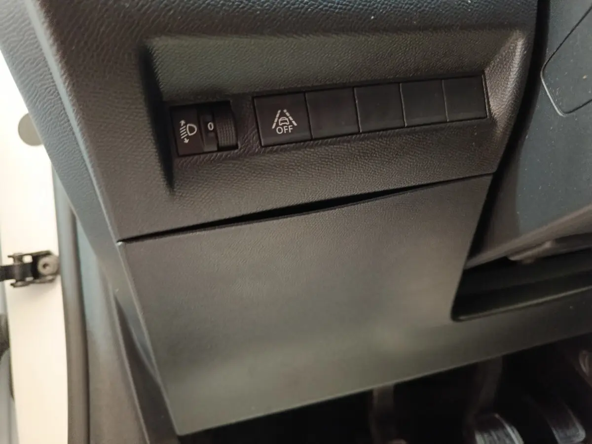 Détail du tableau de bord côté gauche d’un Peugeot 208 blanc, avec commandes de réglage des phares et d’aide au maintien de voie.