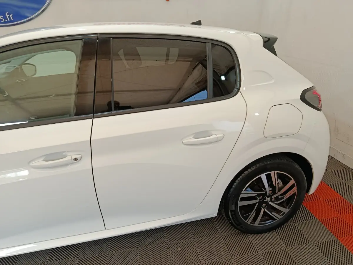 Vue latérale droite sur l'arrière d'une Peugeot 208 blanche avec jante alliage et vitres teintées.