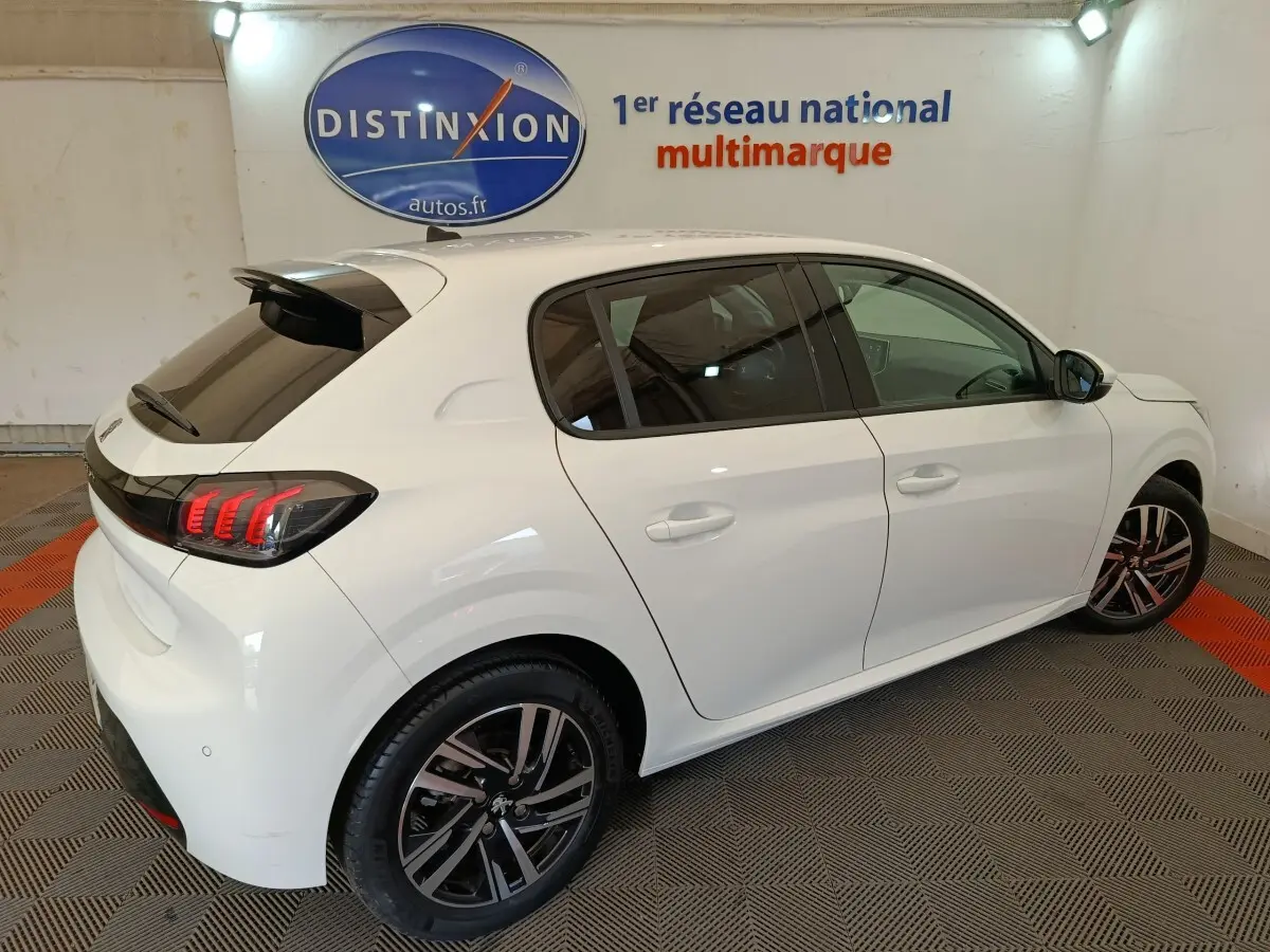 Peugeot 208 blanc vue 3/4 arrière droit, feux arrière à griffes LED et jantes alliage noires visibles.