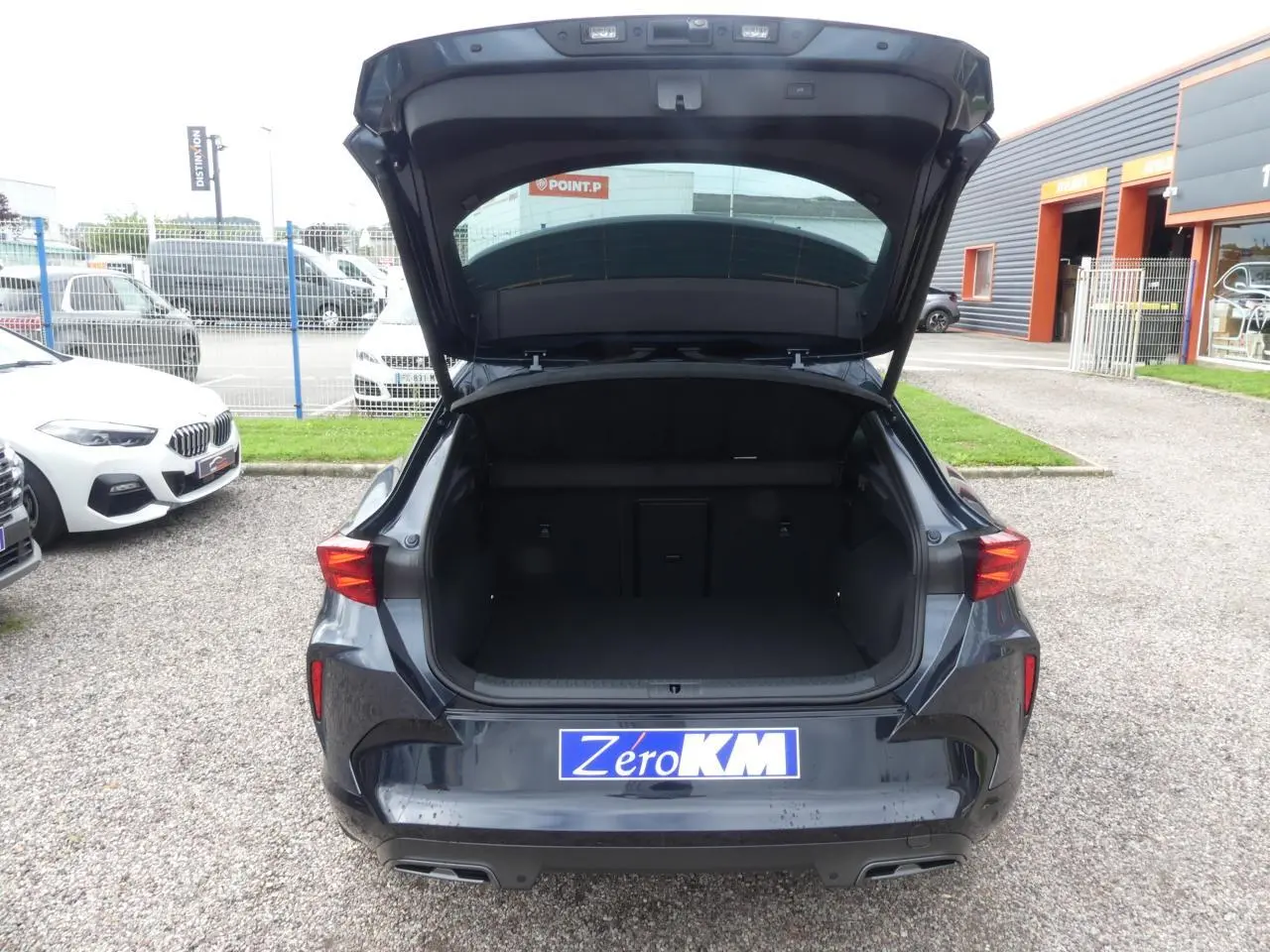 Vue arrière du CUPRA Formentor gris magnétique 2025 avec coffre ouvert et feux arrière allumés dans un parking.
