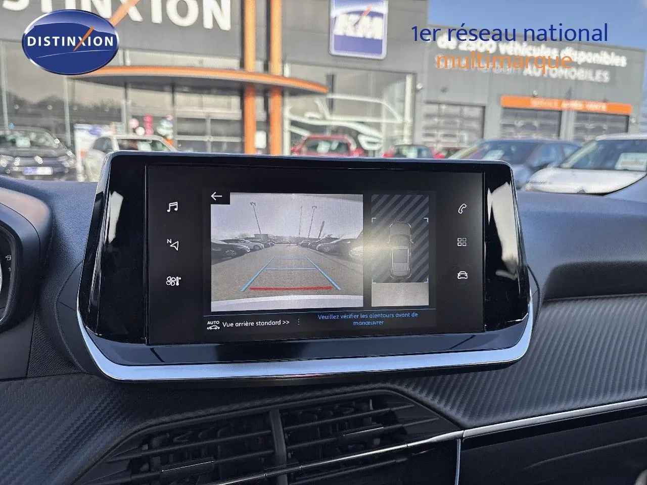 Écran tactile central affichant la caméra de recul d'un Peugeot 2008 gris, avec vue sur parking extérieur.