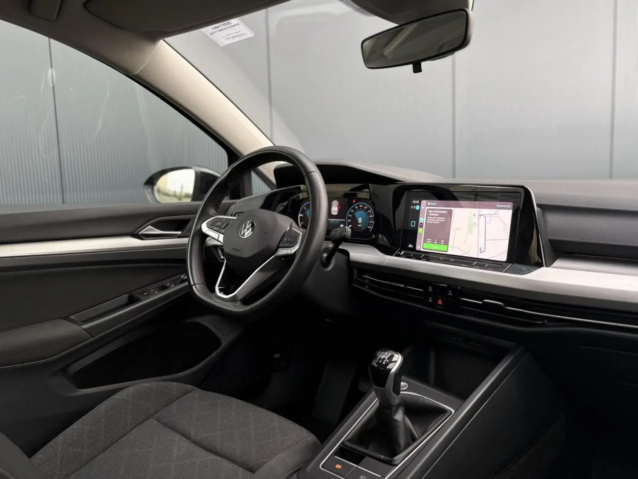 Coffre ouvert d'une Volkswagen Golf VIII noire vue de l'arrière, avec tapis de coffre et banquette arrière visible.