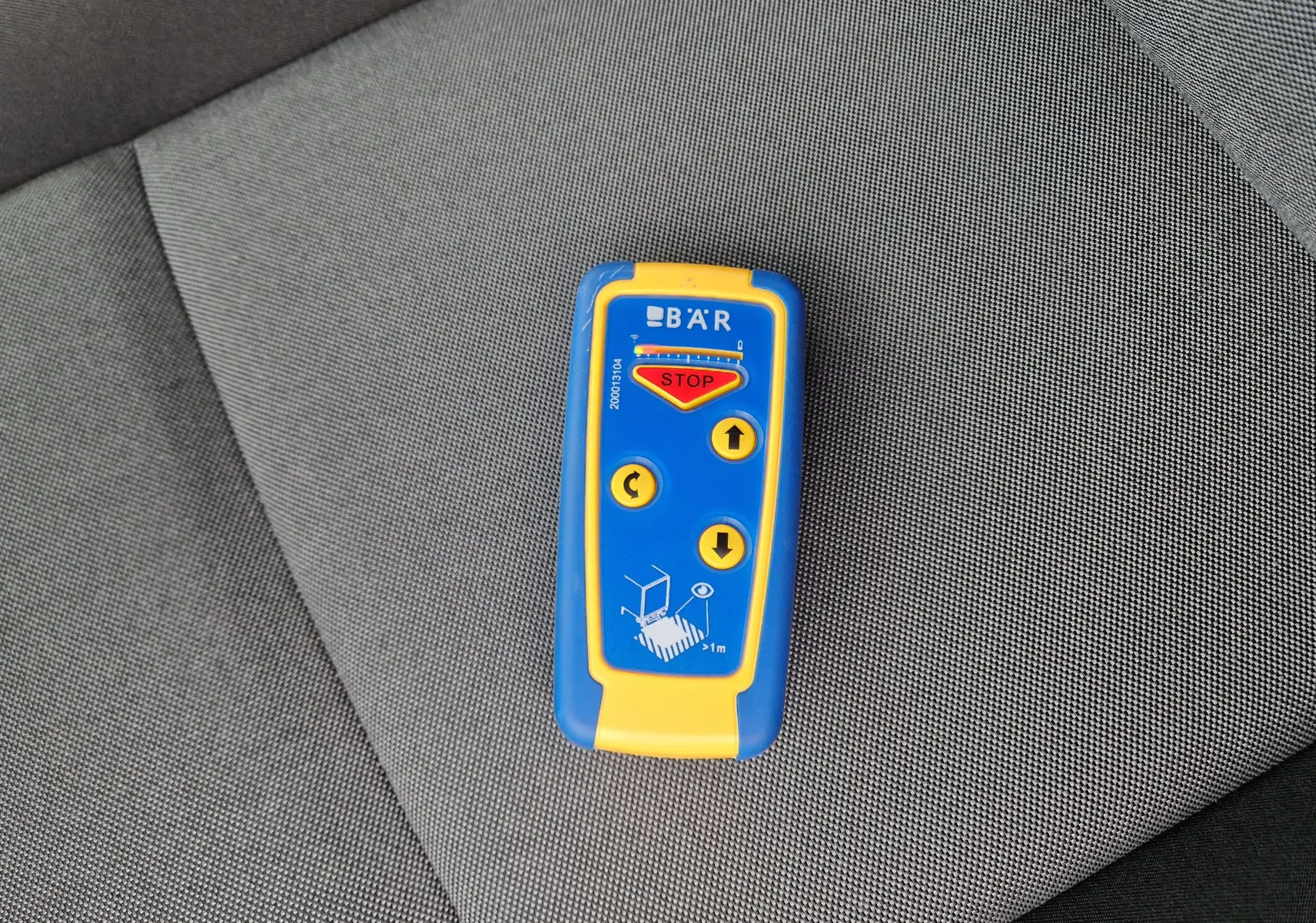 Télécommande bleue et jaune posée sur un siège gris à l'intérieur du Renault Master L2H2 blanc 2023.