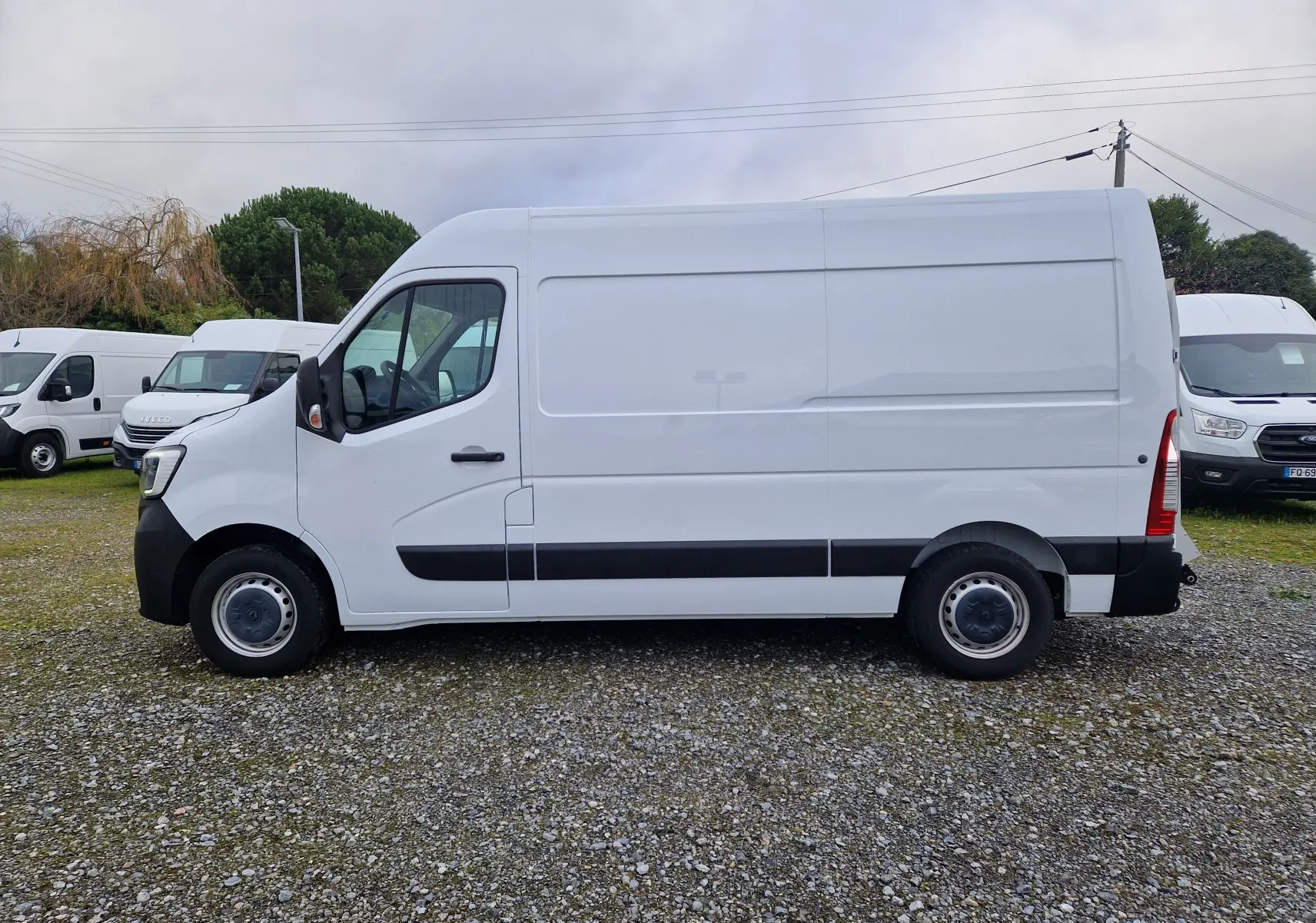 Profil latéral gauche d’un utilitaire Renault Master blanc L2H2 3T3 avec hayon, stationné sur un sol gravillonné.