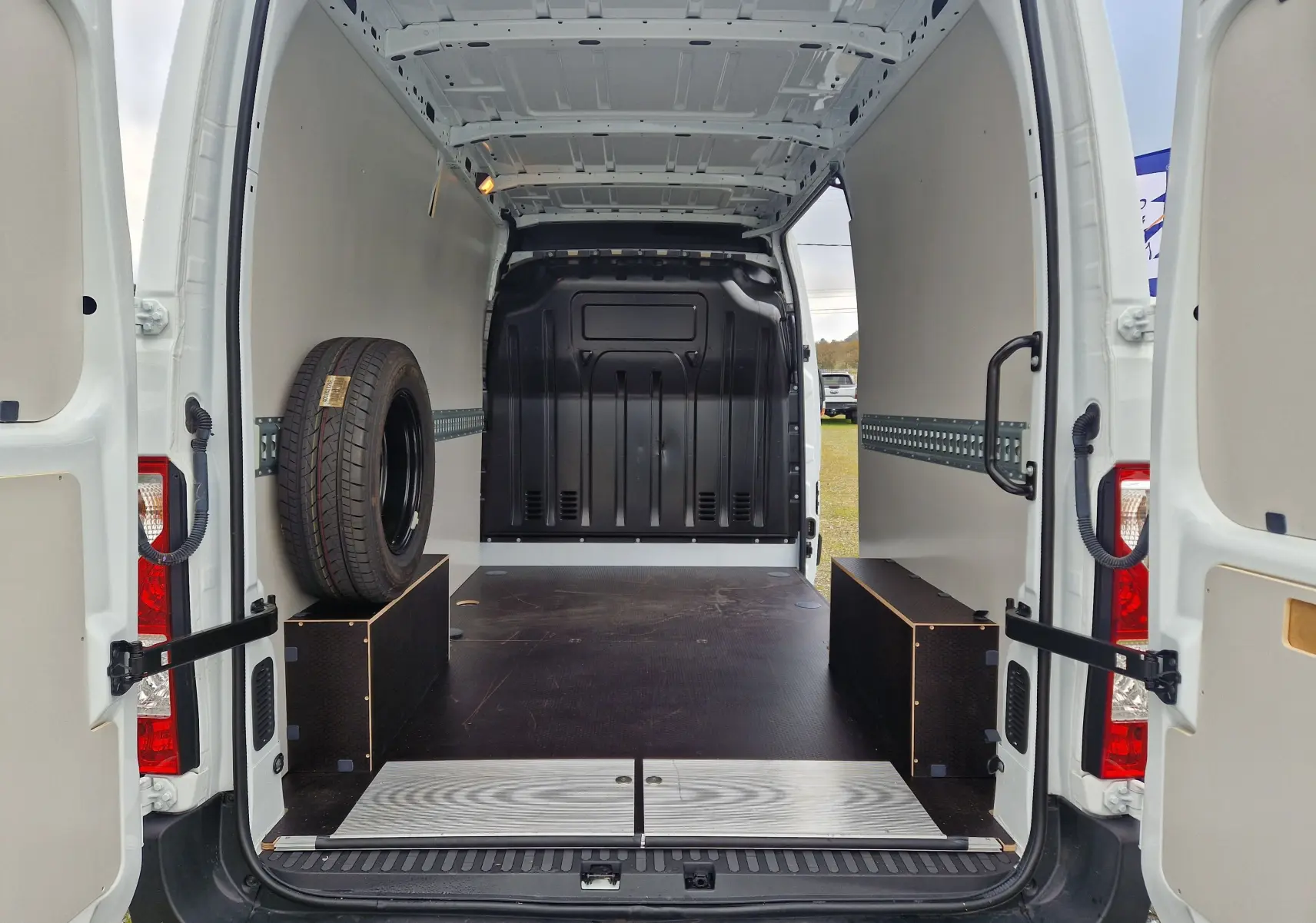 Vue arrière intérieure du Renault Master blanc 2023 avec hayon ouvert et aménagement bois dans l’espace de chargement.