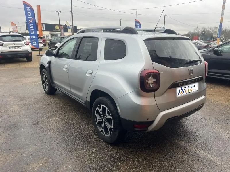 Vue 3/4 arrière droite d'un Dacia Duster gris Comète métallisé avec barres de toit et vitres arrière surteintées