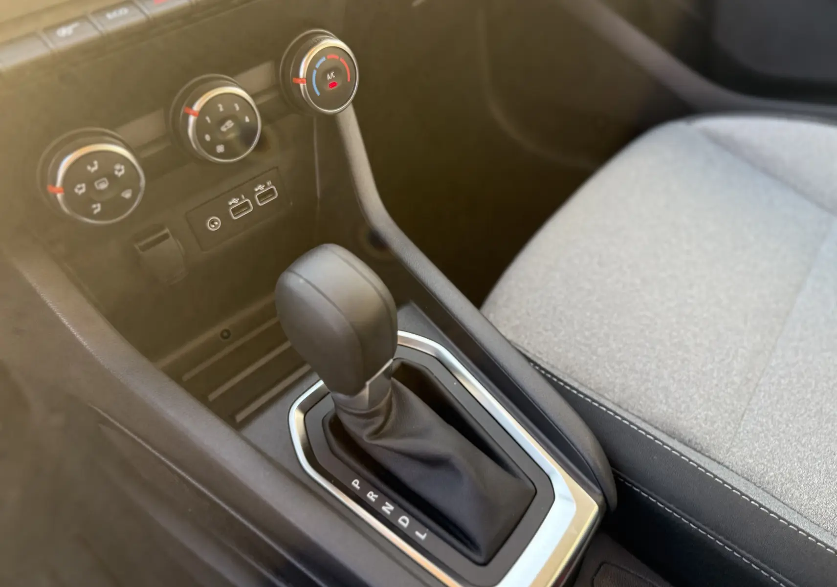 Gros plan sur la console centrale de la Renault Clio V 2025, boîte auto, avec commandes climatisation et siège tissu gris clair.