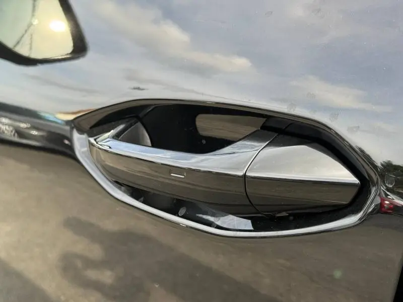 Poignée de porte noire brillante en gros plan sur Audi Q3 2026 Noir Mythique métallisé, reflet du ciel visible.
