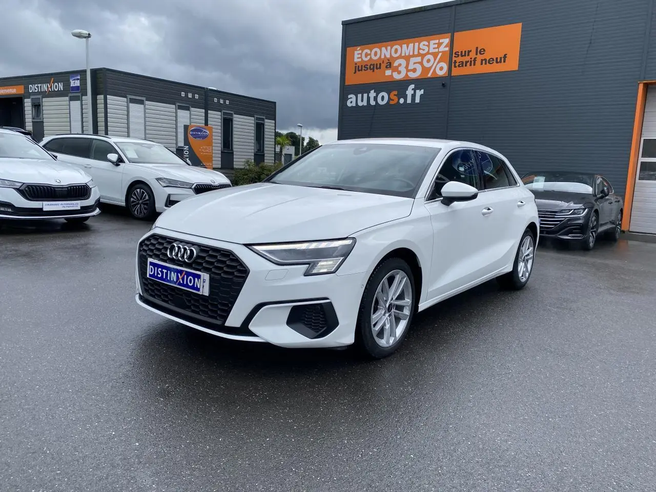 Audi A3 Sportback blanc Ibis vue 3/4 avant droit avec calandre noire et jantes alliage 18 pouces sur parking humide