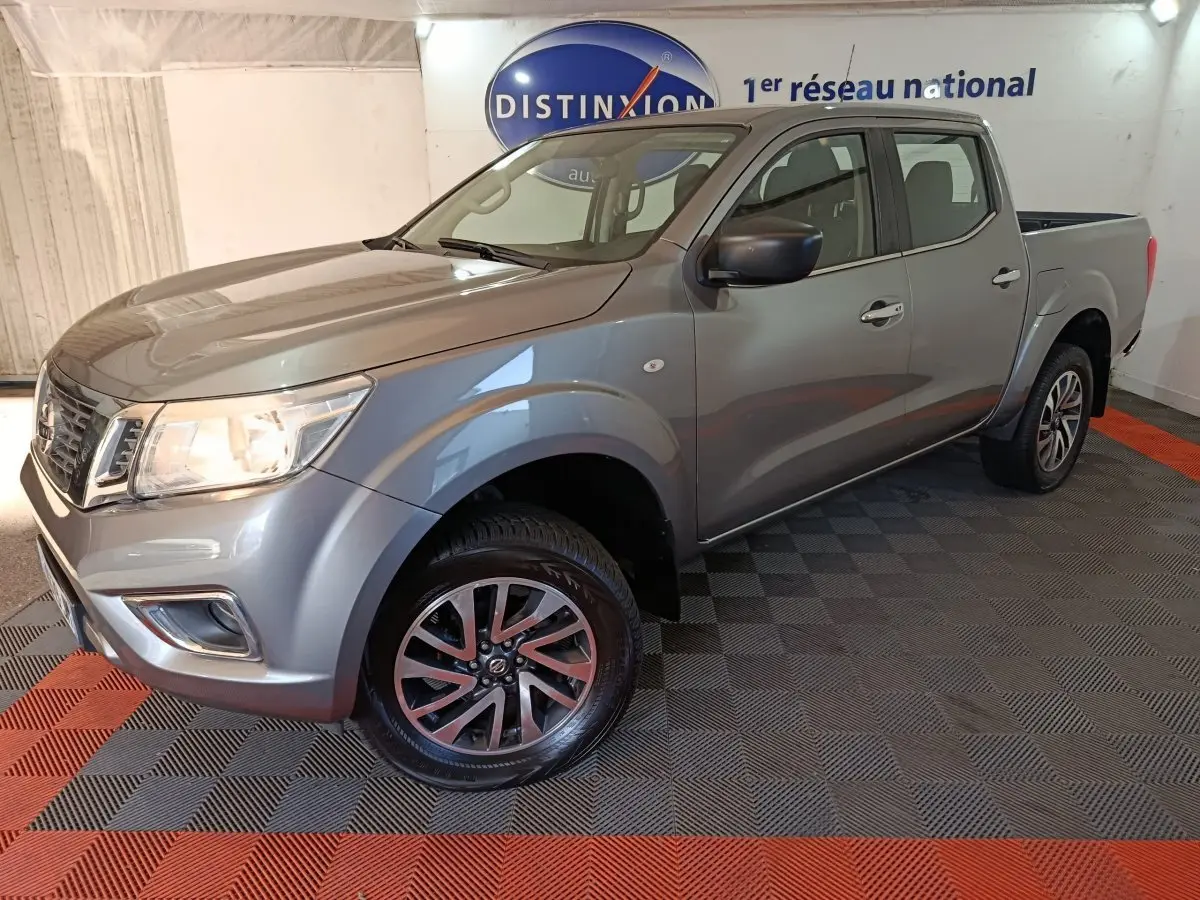 Nissan Navara Double-Cab gris clair vu en 3/4 avant droit, avec jantes alliage et benne pick-up visible.