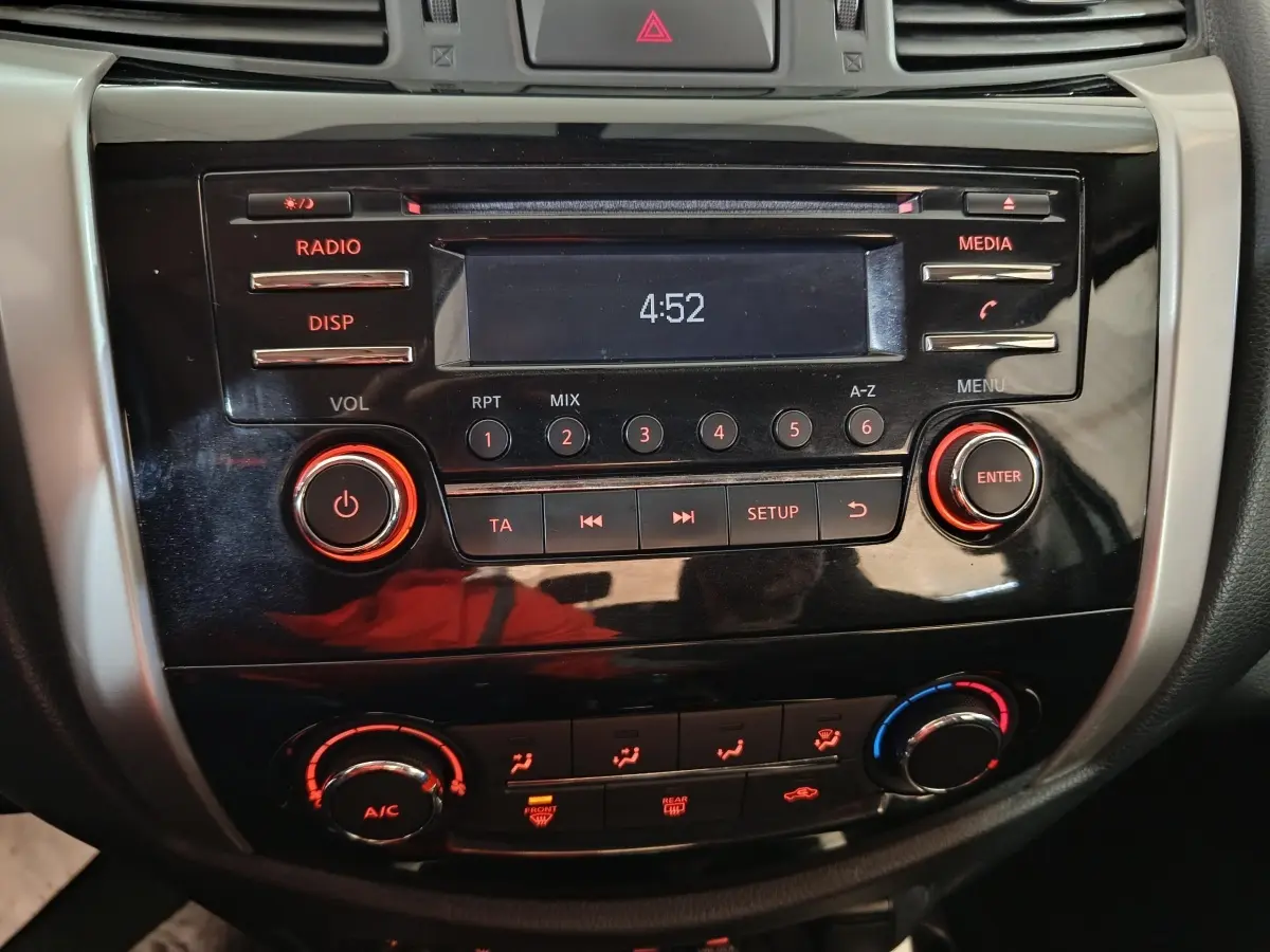 Vue rapprochée du tableau de bord noir du Nissan Navara 2018 avec commandes audio et climatisation éclairées en rouge.