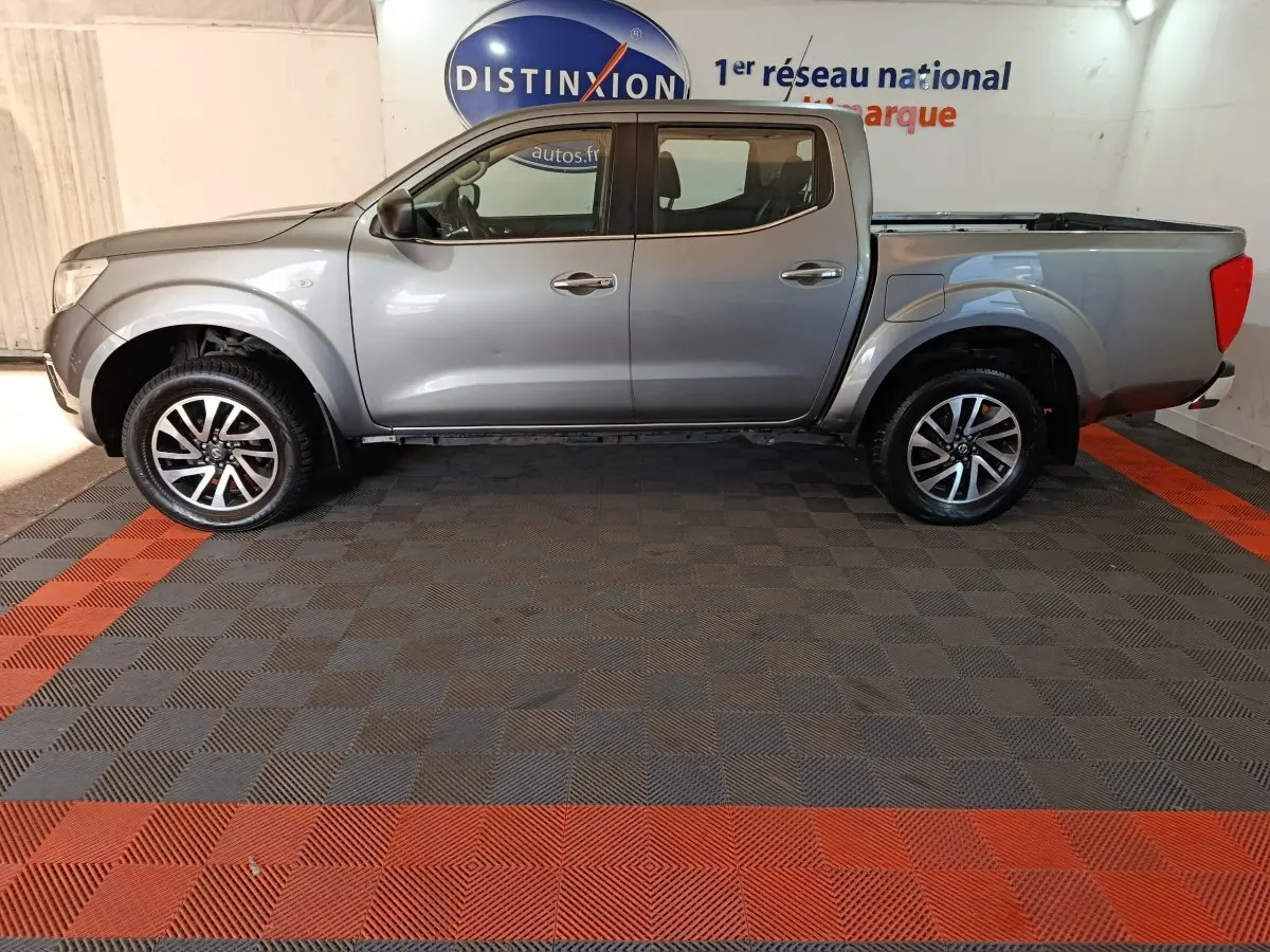 Vue de profil côté gauche d'un Nissan Navara Double-Cab gris clair avec benne pick-up et jantes alliage.