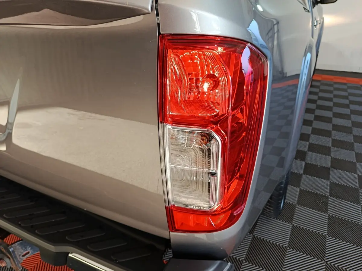 Gros plan sur le feu arrière droit rouge et blanc du Nissan Navara gris clair, avec marchepied noir visible dessous.